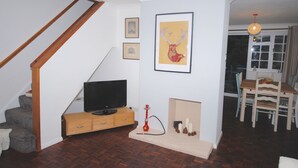 Una sala de estar con televisor, aparador de madera, chimenea y comedor con sillas y mesa.