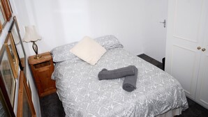 Una cama bien tendida con una colcha estampada, una toalla enrollada, una lámpara de noche y una mesita de madera.
