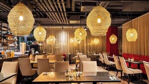 Un interior de restaurante con lámparas colgantes redondas de fibra trenzada, mesas de madera y asientos tapizados en rojo.