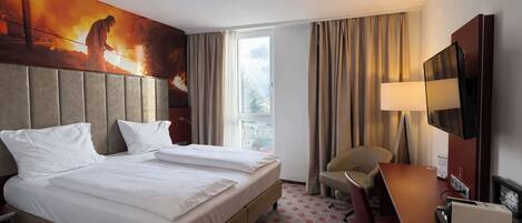 Habitación de hotel con una cama grande, un escritorio, una silla, un televisor y una ventana con cortinas.