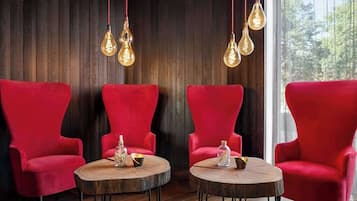 A room with three red armchairs and two round wooden tables, each with a glass jar and a small bowl.