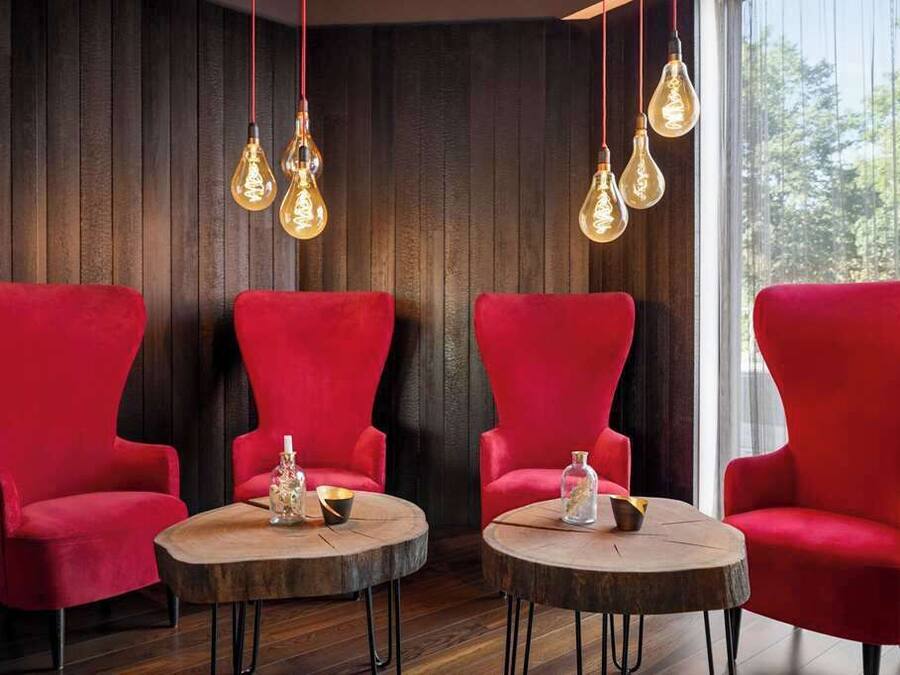 Una habitación con tres sillones rojos y dos mesas redondas de madera, cada una con un tarro de vidrio y un cuenco pequeño.