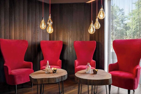 Una habitación con tres sillones rojos y dos mesas redondas de madera, cada una con un tarro de vidrio y un cuenco pequeño.