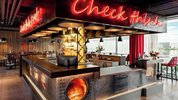 Un área de bar moderna con un letrero de neón, una barra central y diferentes disposiciones de asientos.