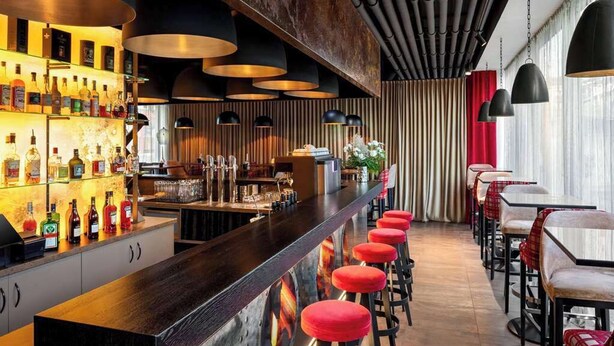 Zona de bar con una barra larga, taburetes rojos y una variedad de botellas de licor.