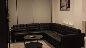 A modern living room with a black leather sectional sofa, a small round coffee table, and a wall-mounted artwork. - MD Luxury Apartment (London)