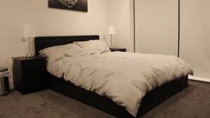 A bedroom with a bed, two bedside tables, a lamp on each table, a trash can, and a painting on the wall. - MD Luxury Apartment (London)