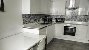 A modern kitchen with white cabinetry, a granite countertop, a built-in oven, and a microwave. - MD Luxury Apartment (London)