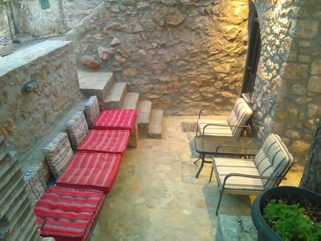 A stone-walled courtyard with a row of red-striped sofas and metal chairs.