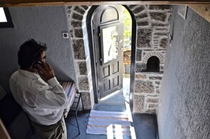 Un hombre habla por teléfono en una habitación con paredes de piedra y una puerta que da al exterior.
