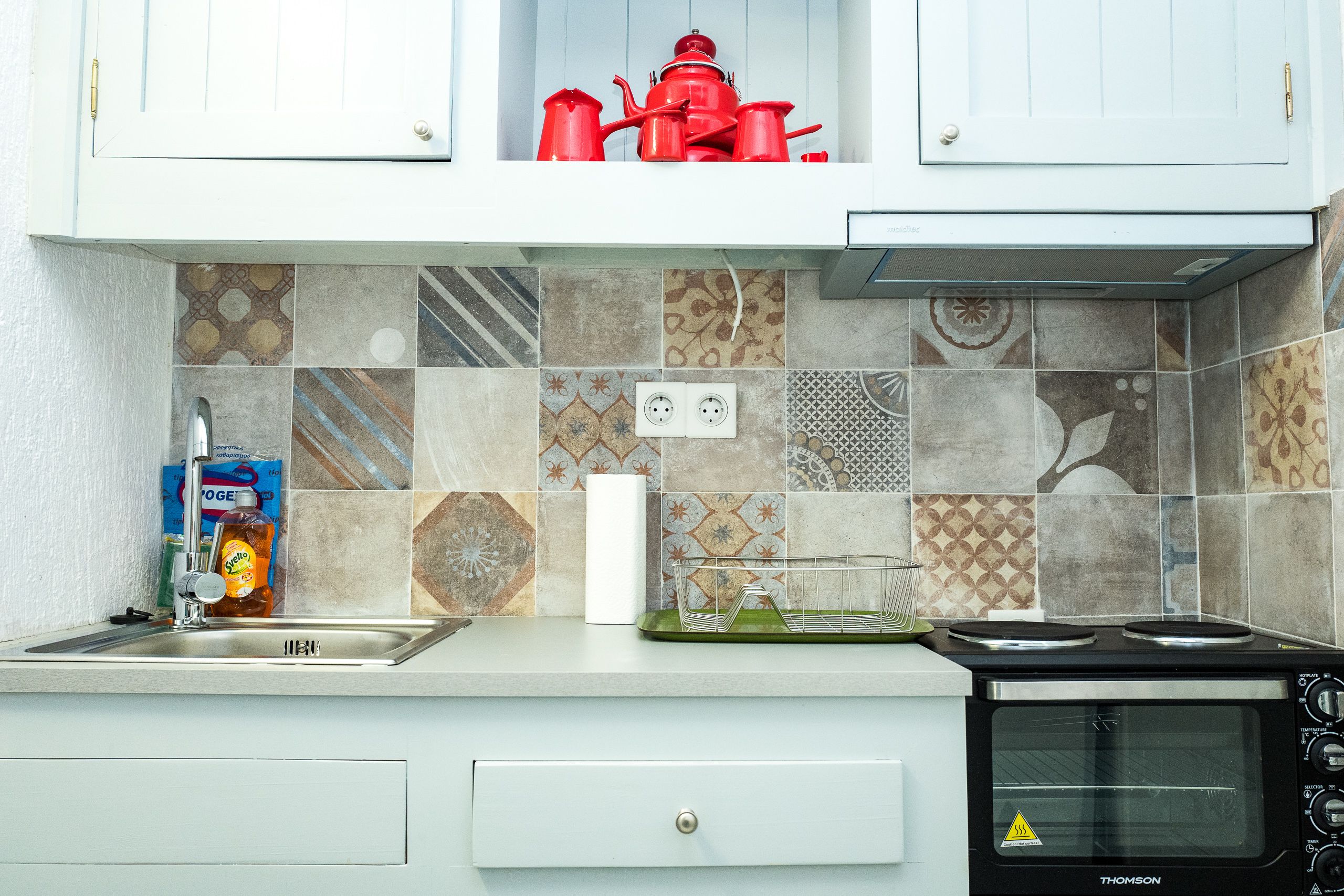 Una cocina con horno empotrado, un lavamanos y diversos azulejos estampados.