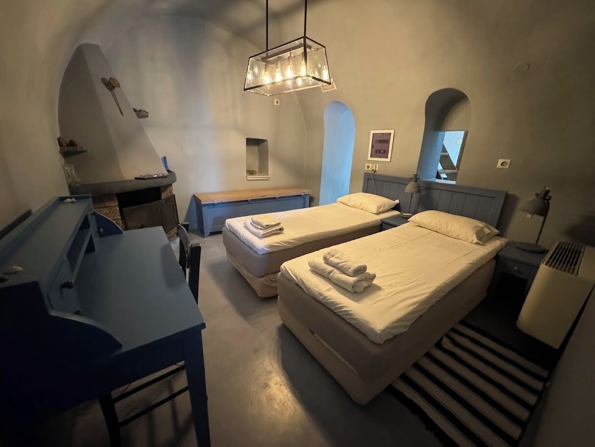 Quarto com duas camas, uma escrivaninha, um espelho e um candeeiro pendente.