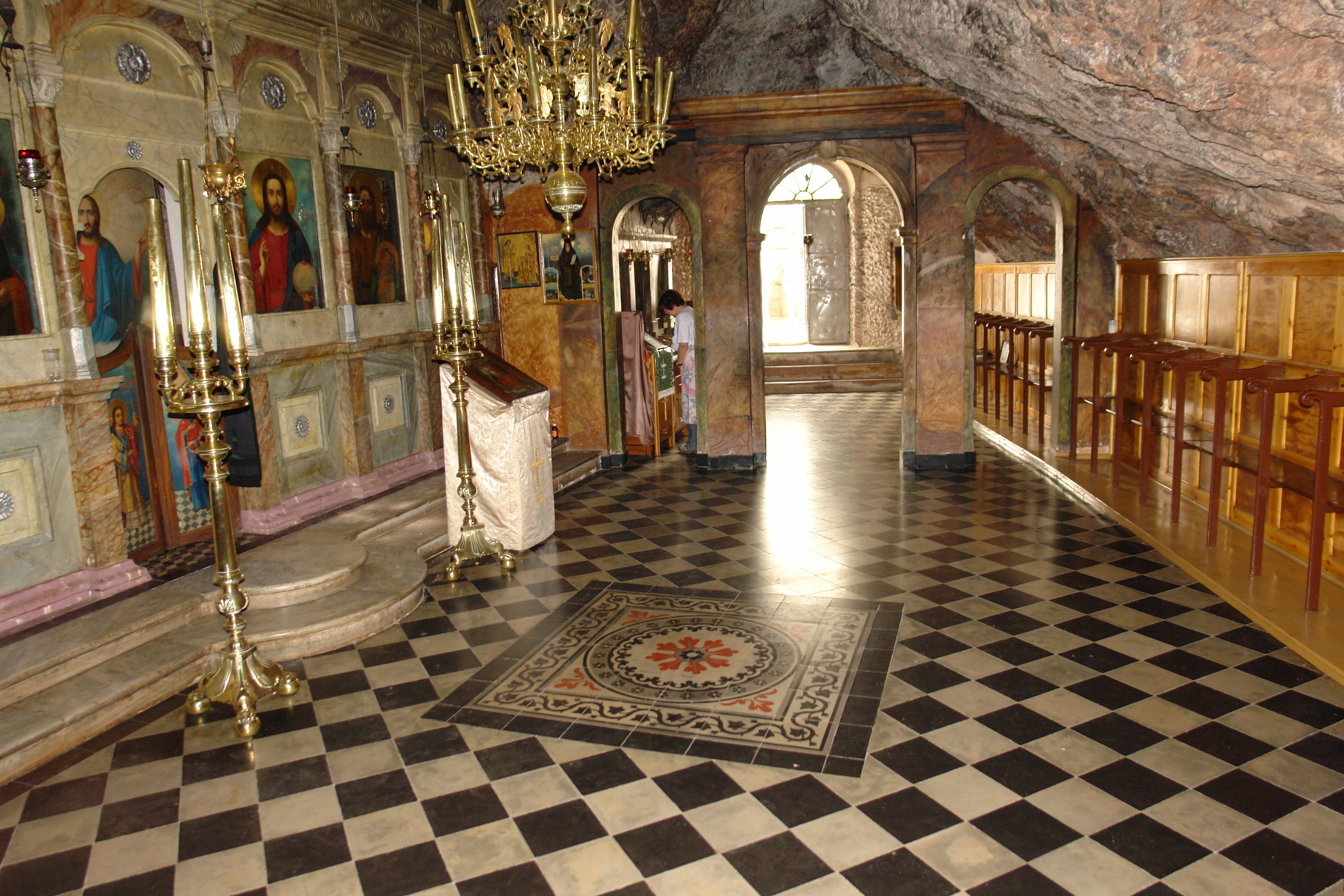 A church interior with checkered flooring, a chandelier, and religious icons.
