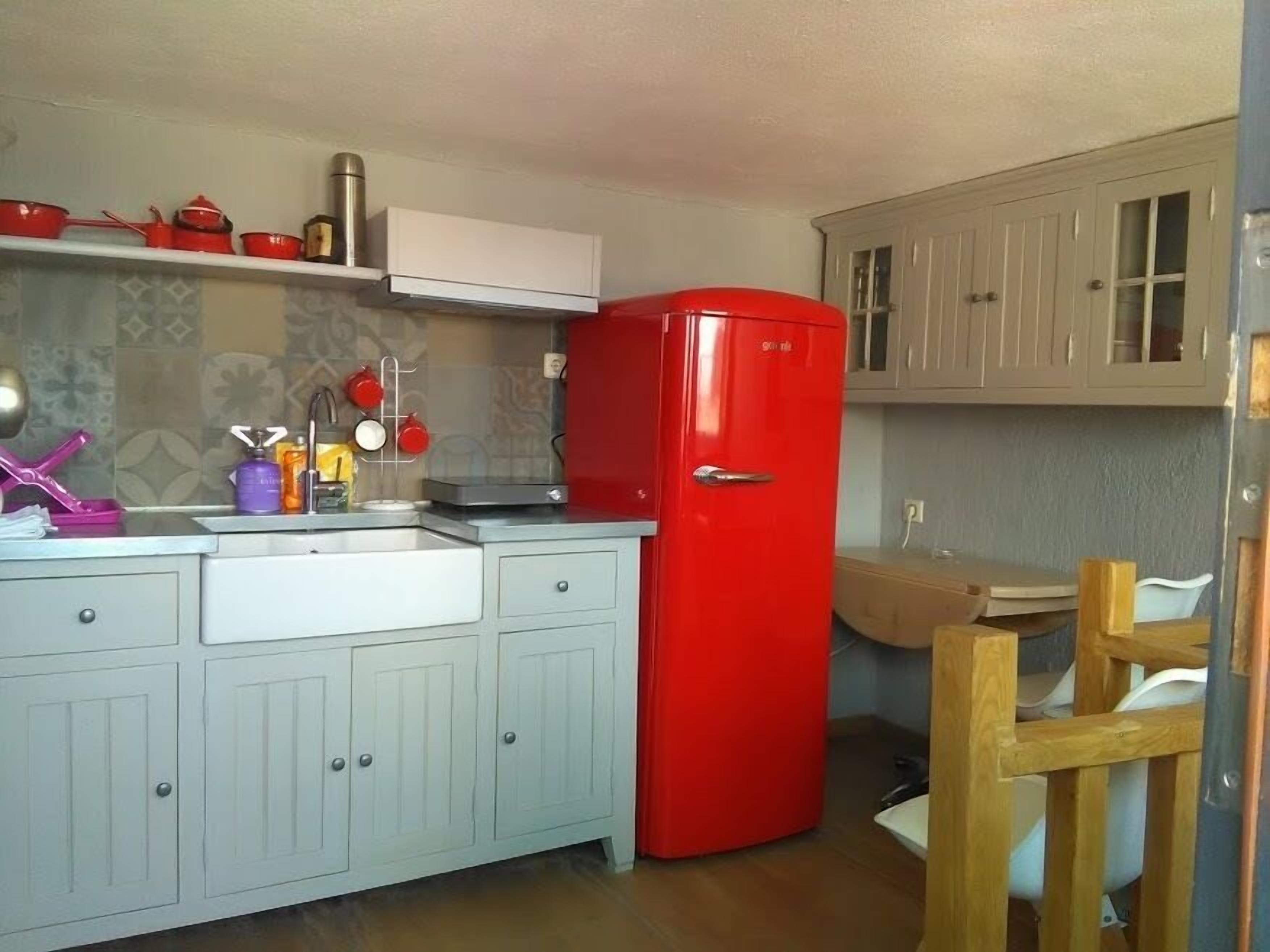 A compact kitchen with a red refrigerator, a sink, and a wooden chair.