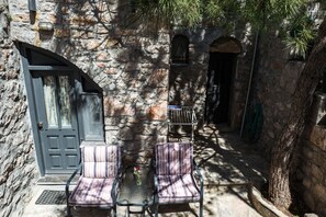 Un patio con paredes de piedra, dos sillas a rayas, una mesa, una puerta y una ventana pequeña.