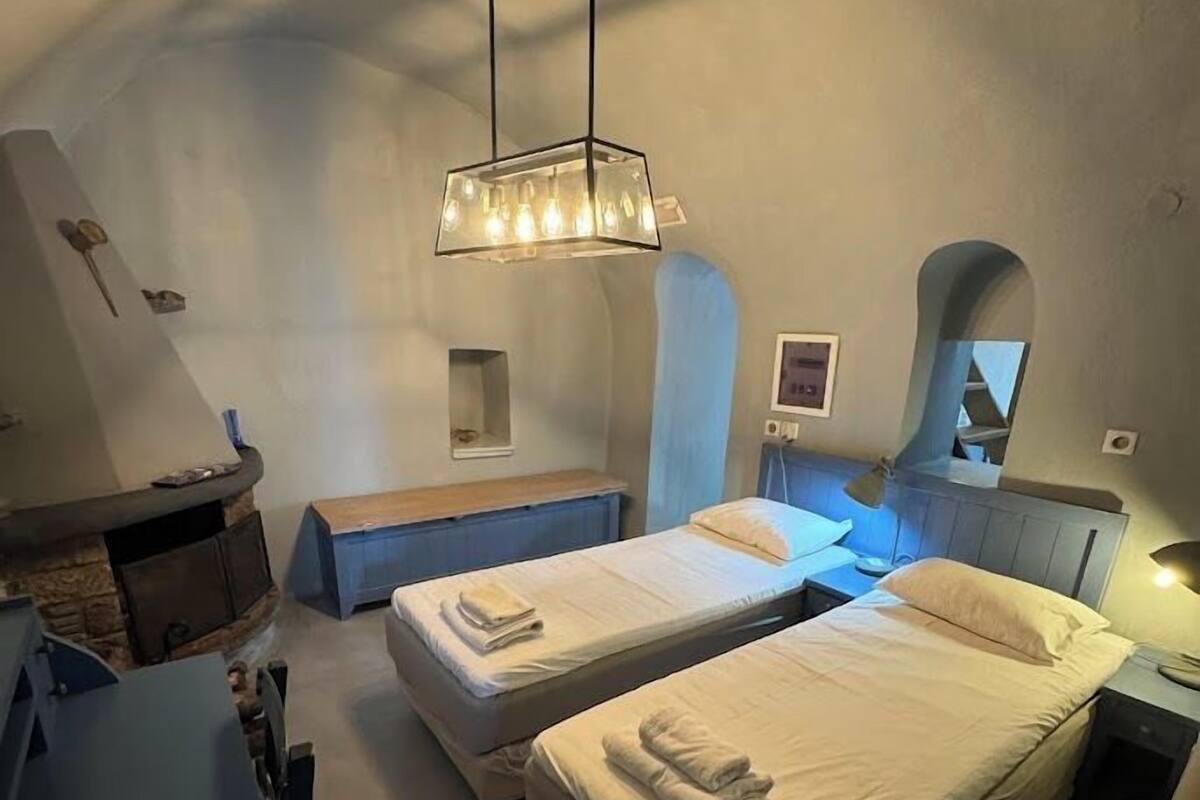 A cozy bedroom with two beds, a bench, a fireplace, and a hanging light fixture.