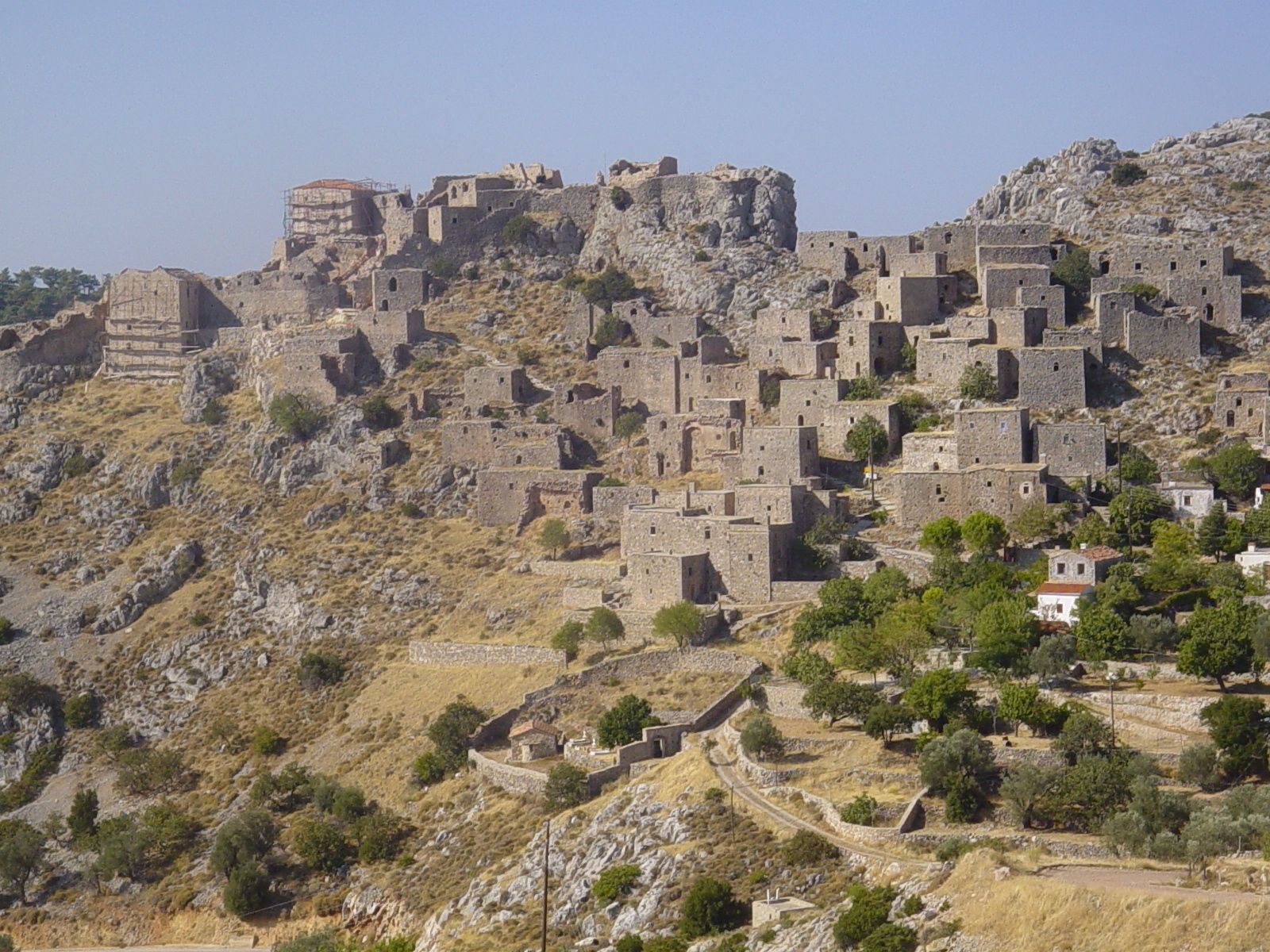 A historic stone fortress with multiple levels and a prominent tower, surrounded by rocky terrain and sparse vegetation.