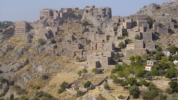 A historic stone fortress with multiple levels and a prominent tower, surrounded by rocky terrain and sparse vegetation.