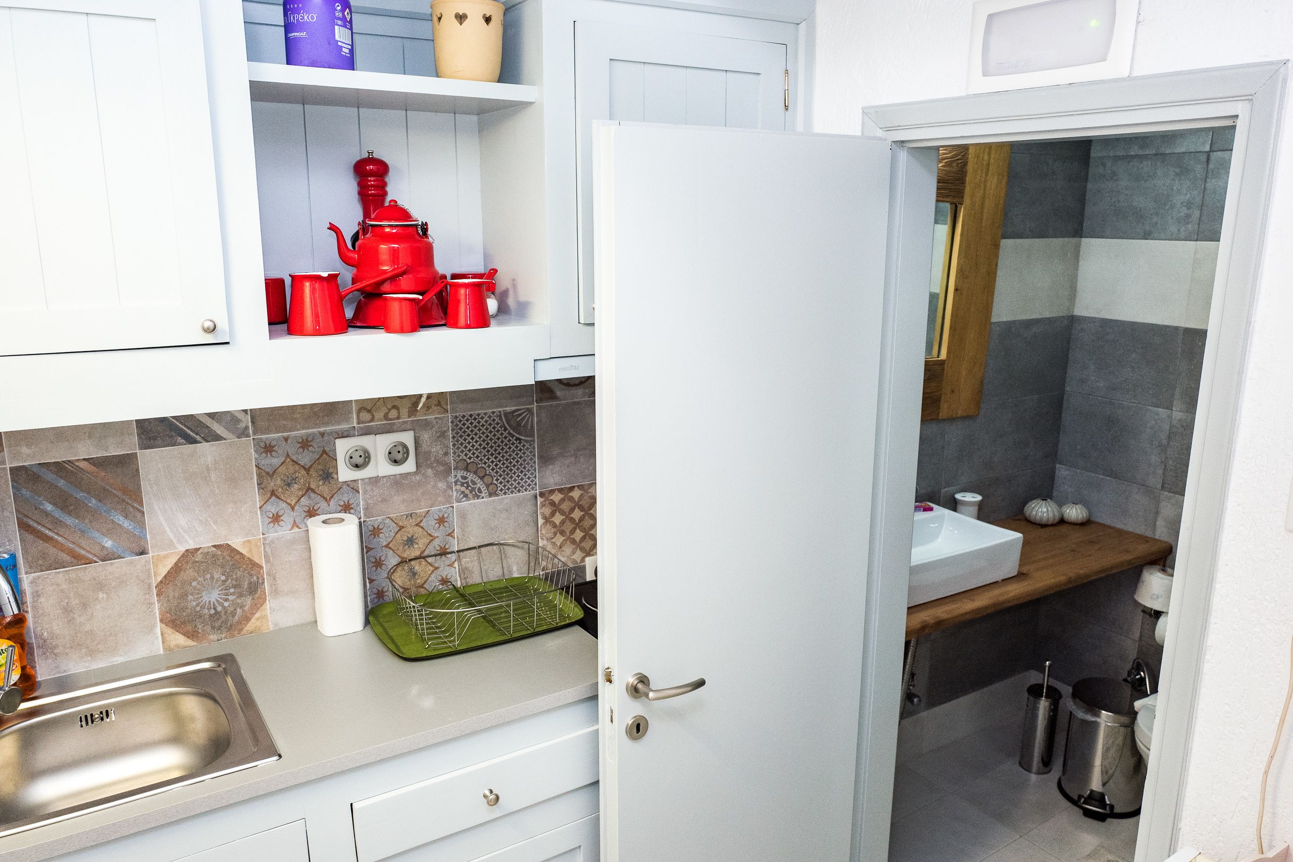 A kitchen with a stainless steel sink, a white door, and a tiled backsplash.