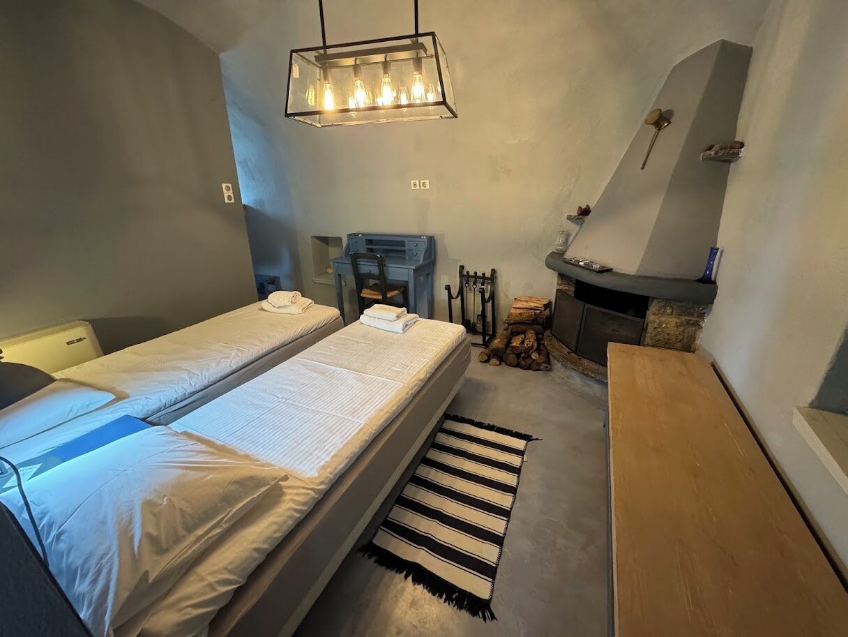 Un dormitorio pequeño y acogedor con dos camas individuales, un banco de madera, una chimenea y una lámpara colgante.
