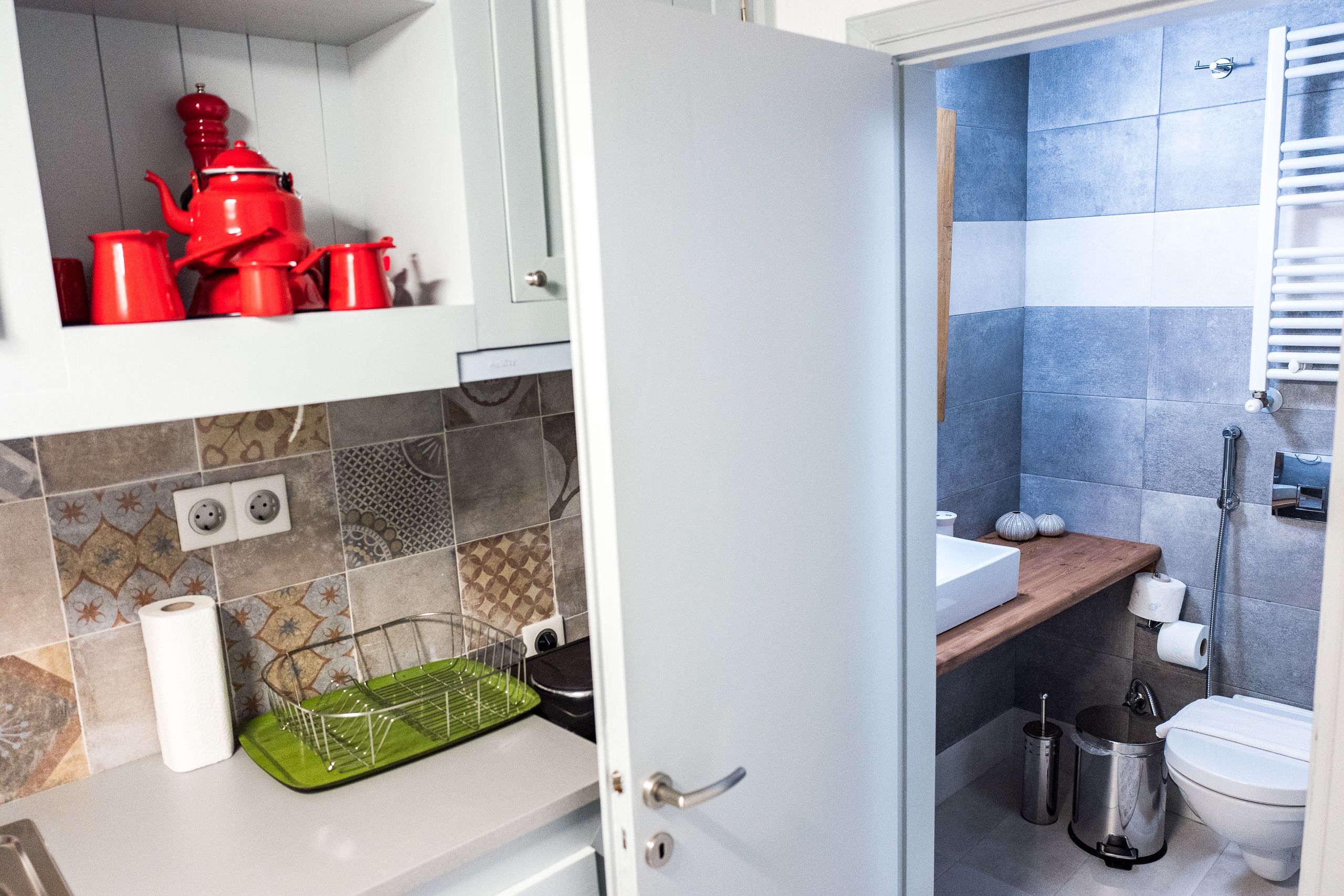Una cocina con un escurreplatos verde, un lavabo blanco y un hervidor rojo.