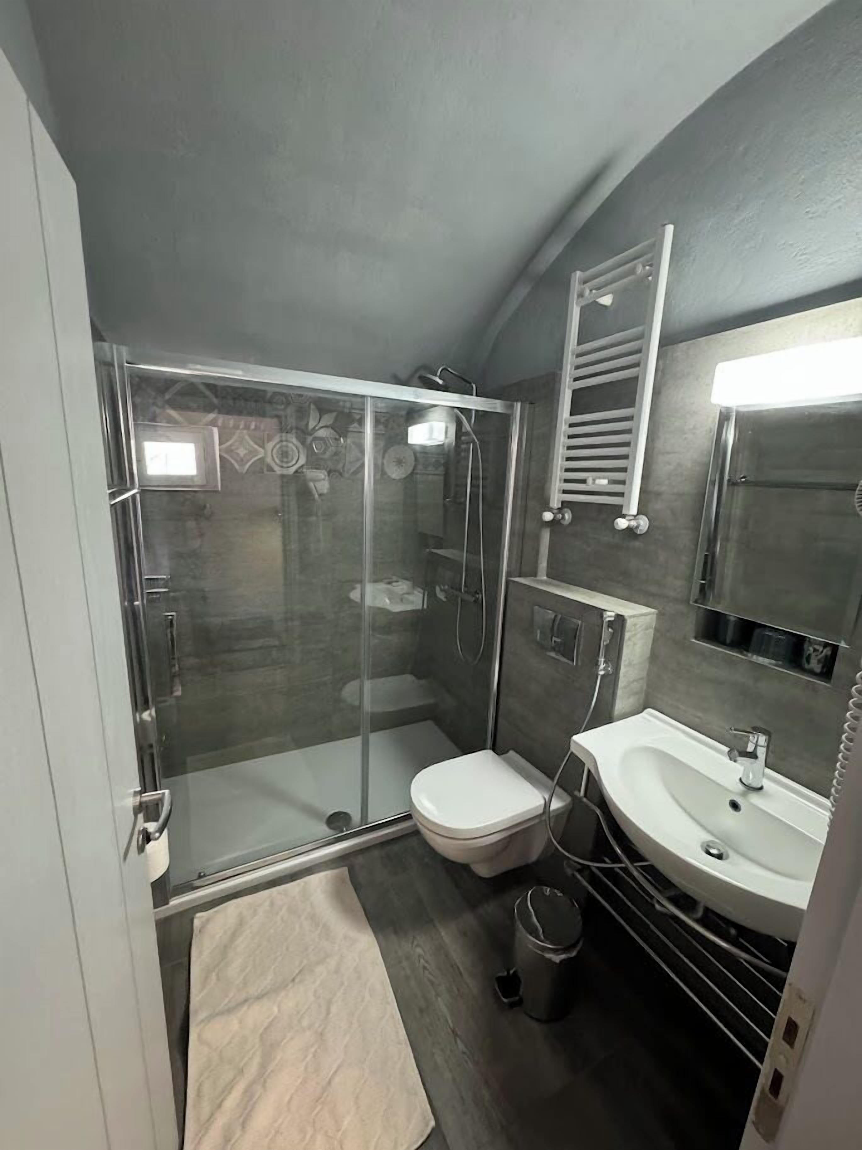 A modern bathroom with a glass-enclosed shower, a white toilet, a sink with a mirror, and a towel rack.