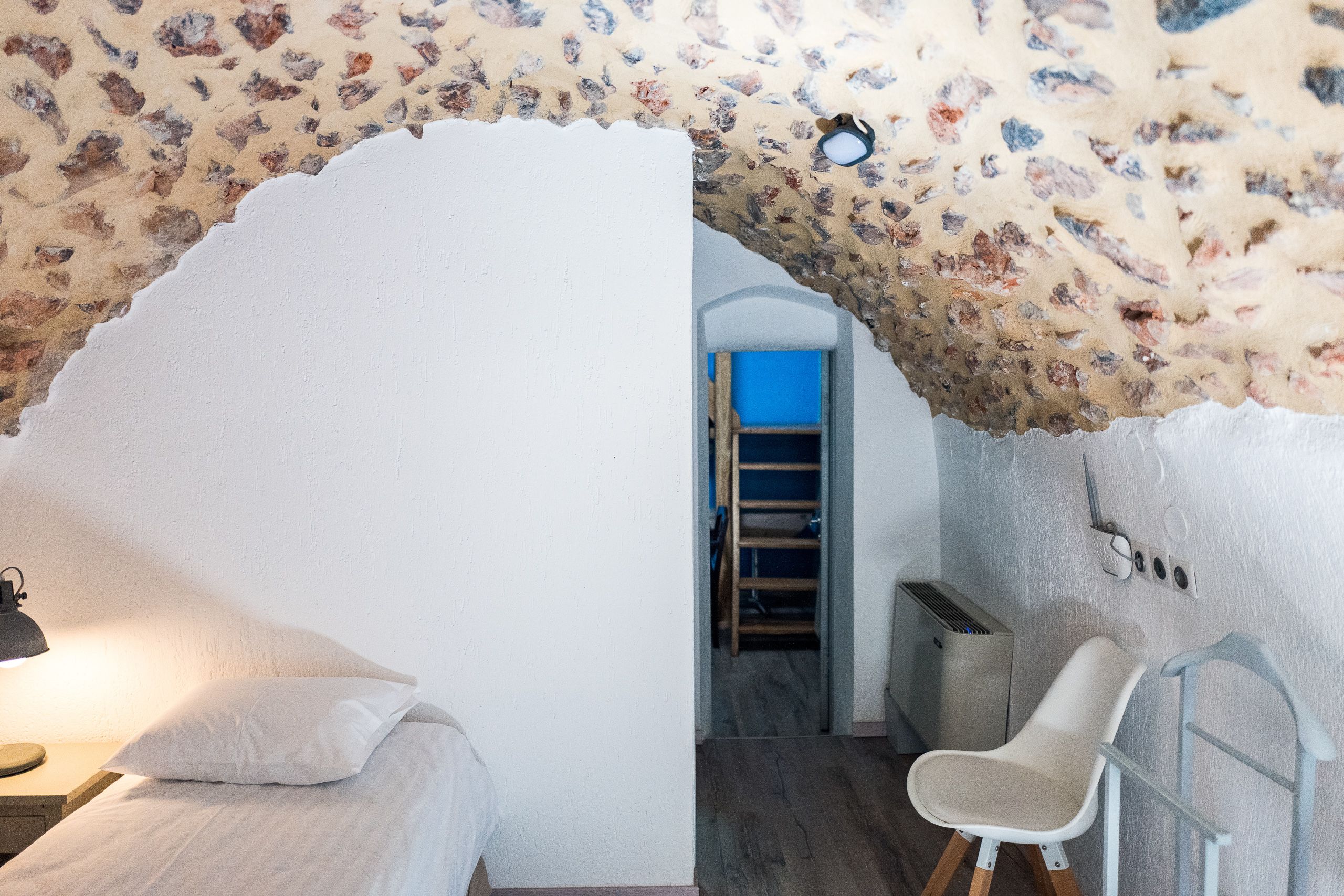 A bedroom with a bed, a chair, a desk, and a ladder leading to a lofted sleeping area.