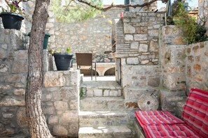 Una escalera de piedra lleva a un espacio cubierto con una silla de mimbre y un banco a rayas rojas.