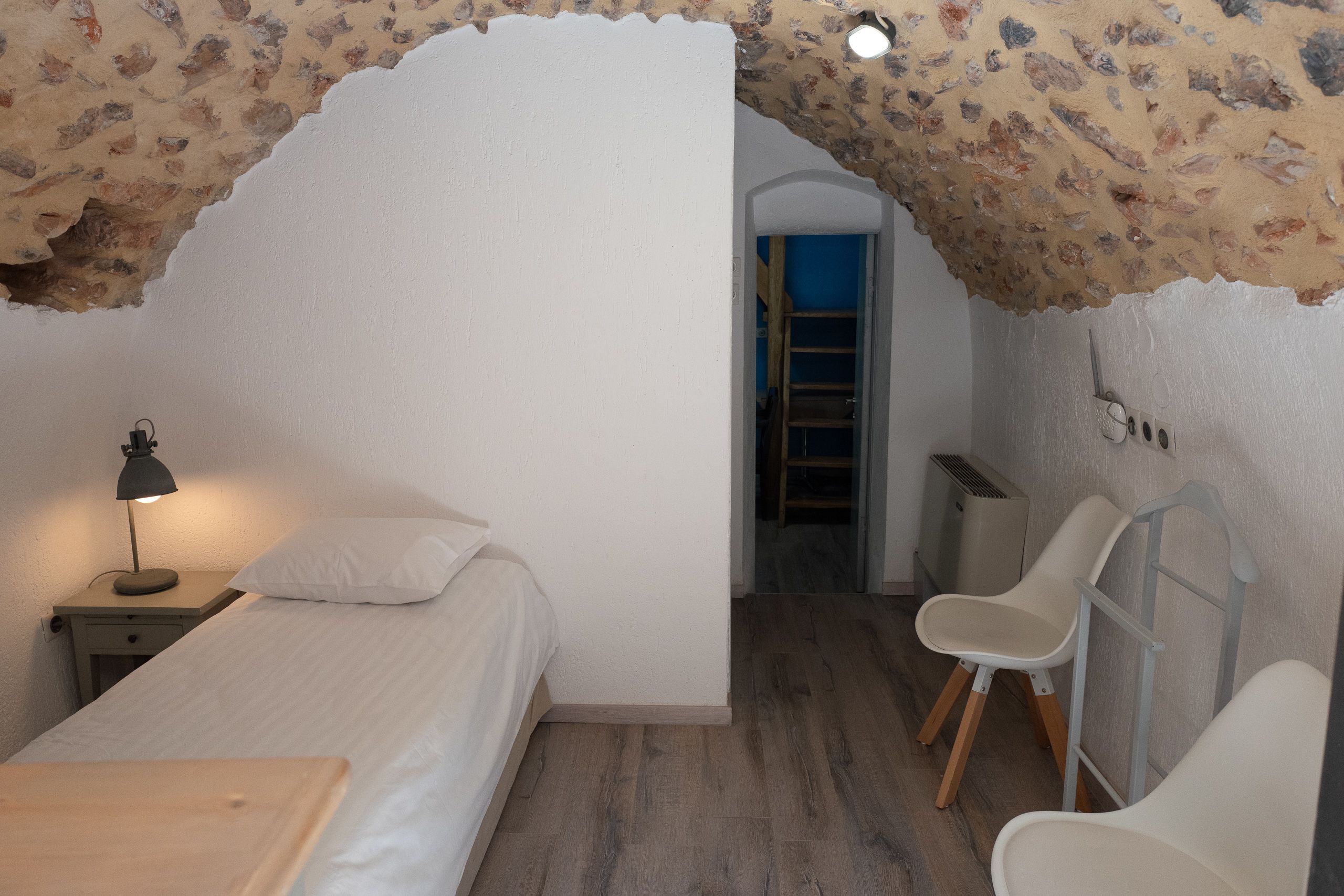 A bedroom with a bed, a nightstand with a lamp, a wooden table, and a chair.