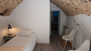 A bedroom with a bed, a nightstand with a lamp, a wooden table, and a chair.