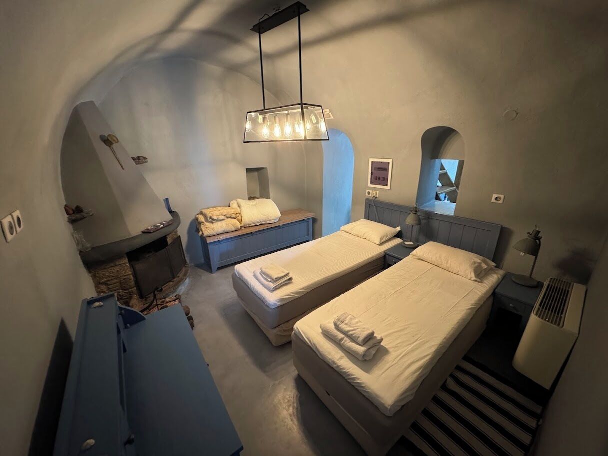 Habitación de hotel compacta con dos camas individuales, un pequeño rincón de descanso, chimenea empotrada y un techo abovedado único.