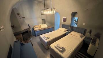Habitación de hotel compacta con dos camas individuales, un pequeño rincón de descanso, chimenea empotrada y un techo abovedado único.
