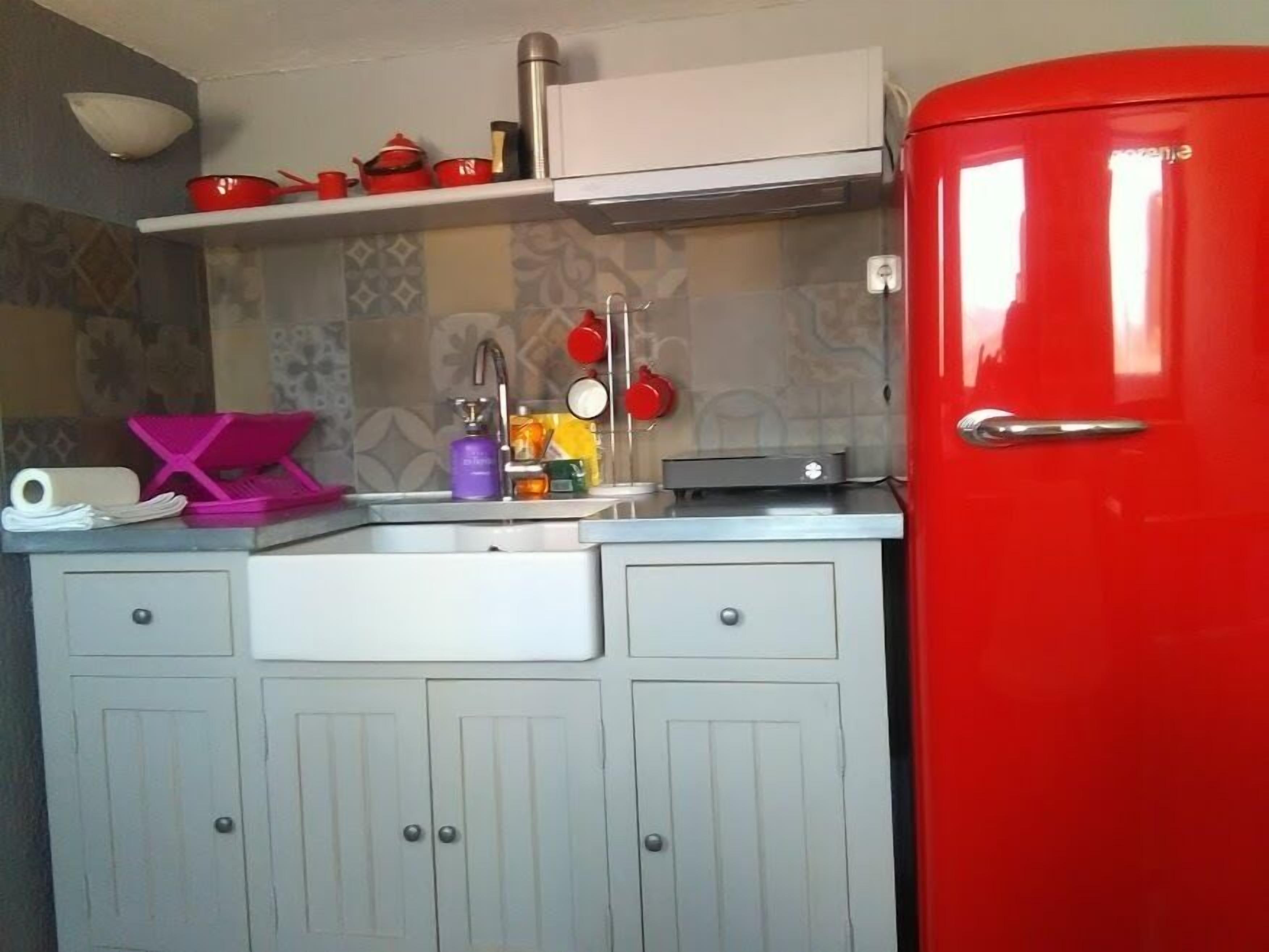 Une cuisine de taille réduite avec un réfrigérateur rouge, un évier contenant divers objets et un meuble blanc.