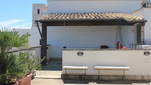 Eine Terrasse im Freien mit einem gefliessten Dach, zwei Bänken und einer weißen Wand mit einem Fenster.