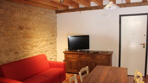 Ein Zimmer mit Steinwand, einem roten Sofa, einem Holzesstisch und einem Fernseher auf einem Schrank.