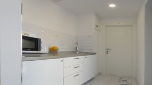 A modern kitchen with white cabinets, a microwave, a sink, and a bowl of fruit. - Central Old Town Rooms (Split)