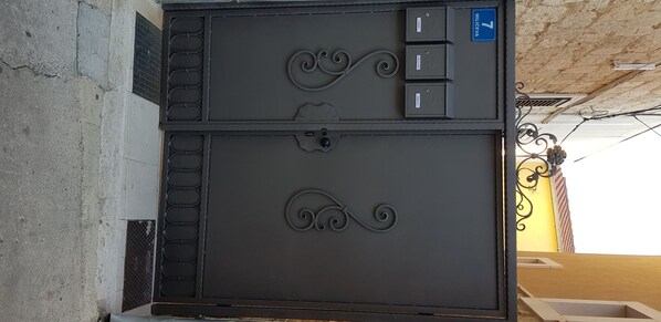 A metal gate with a lock and a keyhole, a blue sign with the number 7, and a metal vent on the wall.