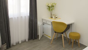 A small, neatly arranged room with a white desk, a yellow chair, a small stool, and a vase with flowers on the desk. - Central Old Town Rooms (Split)