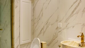 A bathroom with a marble wall, a toilet, a sink with a gold faucet, and a cabinet. - Elegance Hotel (Ulaanbaatar)