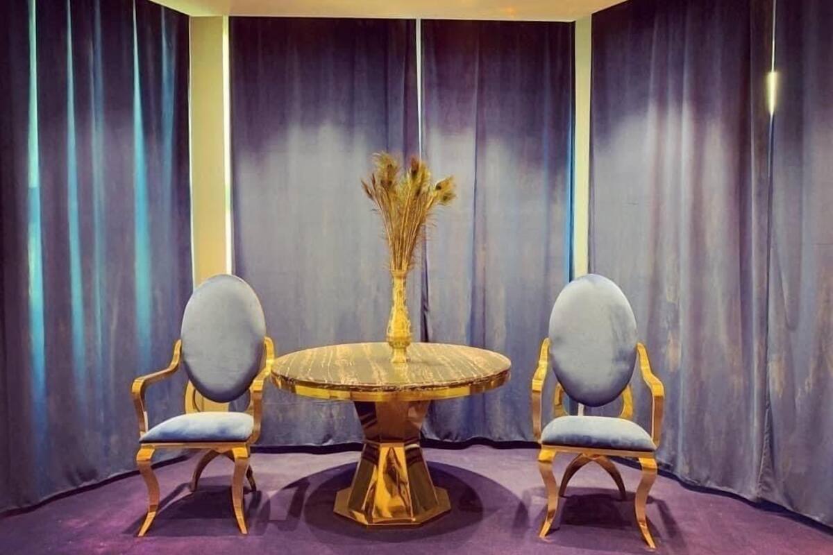 Une pièce avec une table ronde et deux chaises, un vase contenant des fleurs séchées et des rideaux foncés.