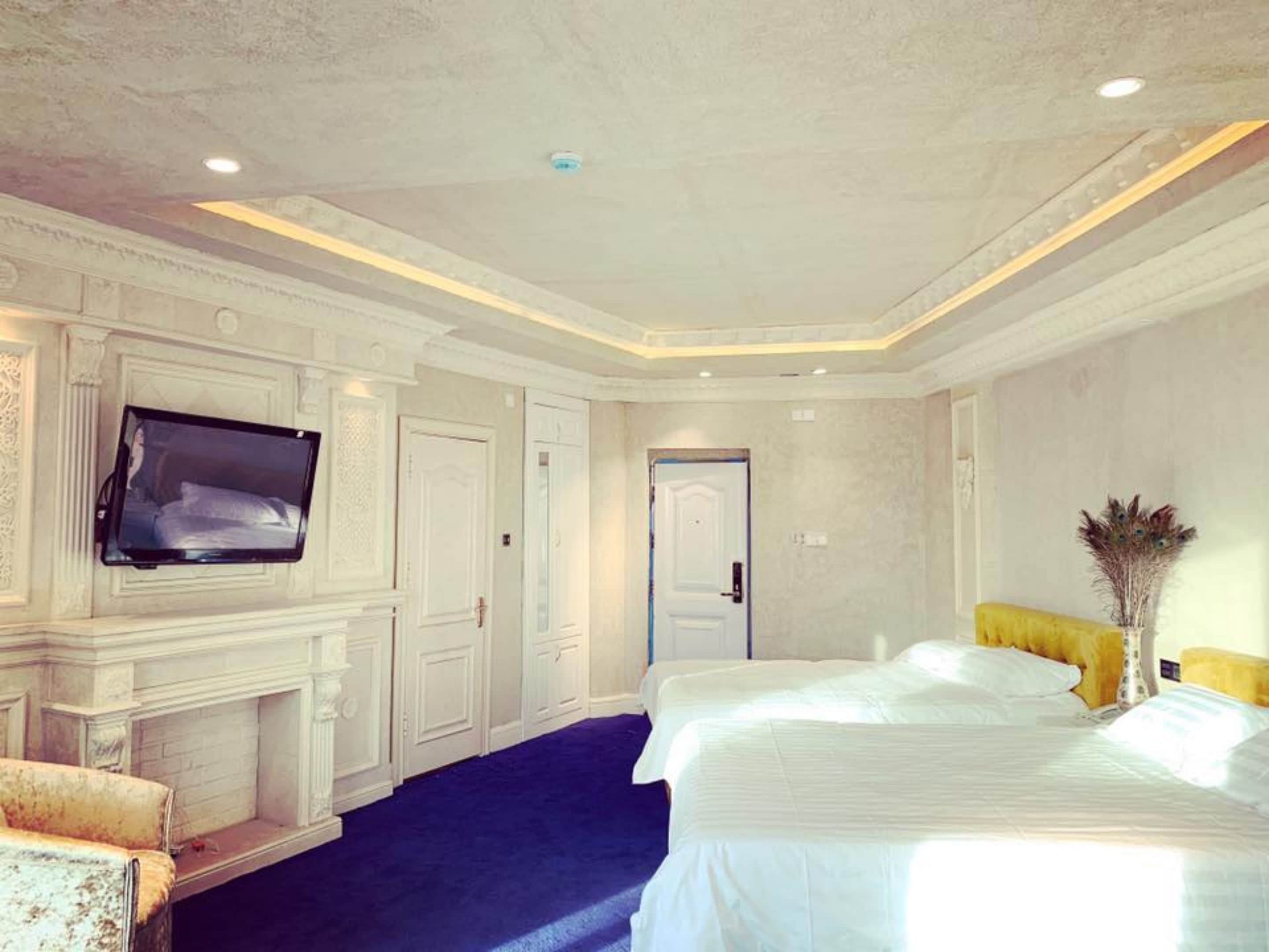 A hotel room with a large bed, a flat-screen TV mounted on the wall, a fireplace, and a door leading to another room.