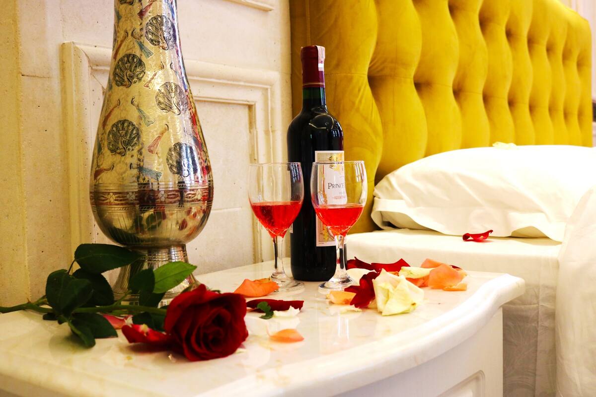 Une table ornée d’un vase décoratif, de deux verres de vin rouge et de pétales de rose éparpillés.