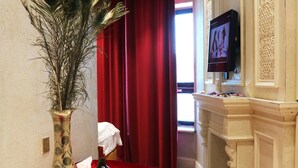 A hotel room with a round table set for two, a vase with a plant, a bottle of wine, and glasses on the table. - Elegance Hotel (Ulaanbaatar)