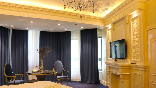 A hotel room with a large bed, two armchairs, a small table with a vase, and a television on the wall. - Elegance Hotel (Ulaanbaatar)