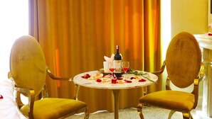 A hotel room with a round table set for two, a bottle of wine, and rose petals on the table. - Elegance Hotel (Ulaanbaatar)