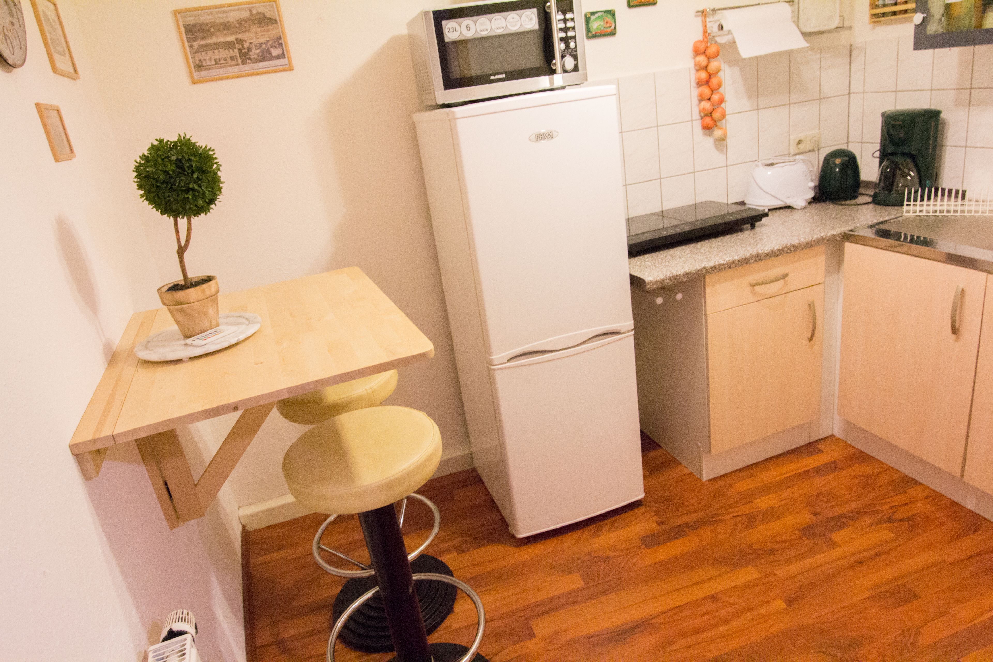 A compact kitchen with a refrigerator, microwave, and a small dining area with a stool.
