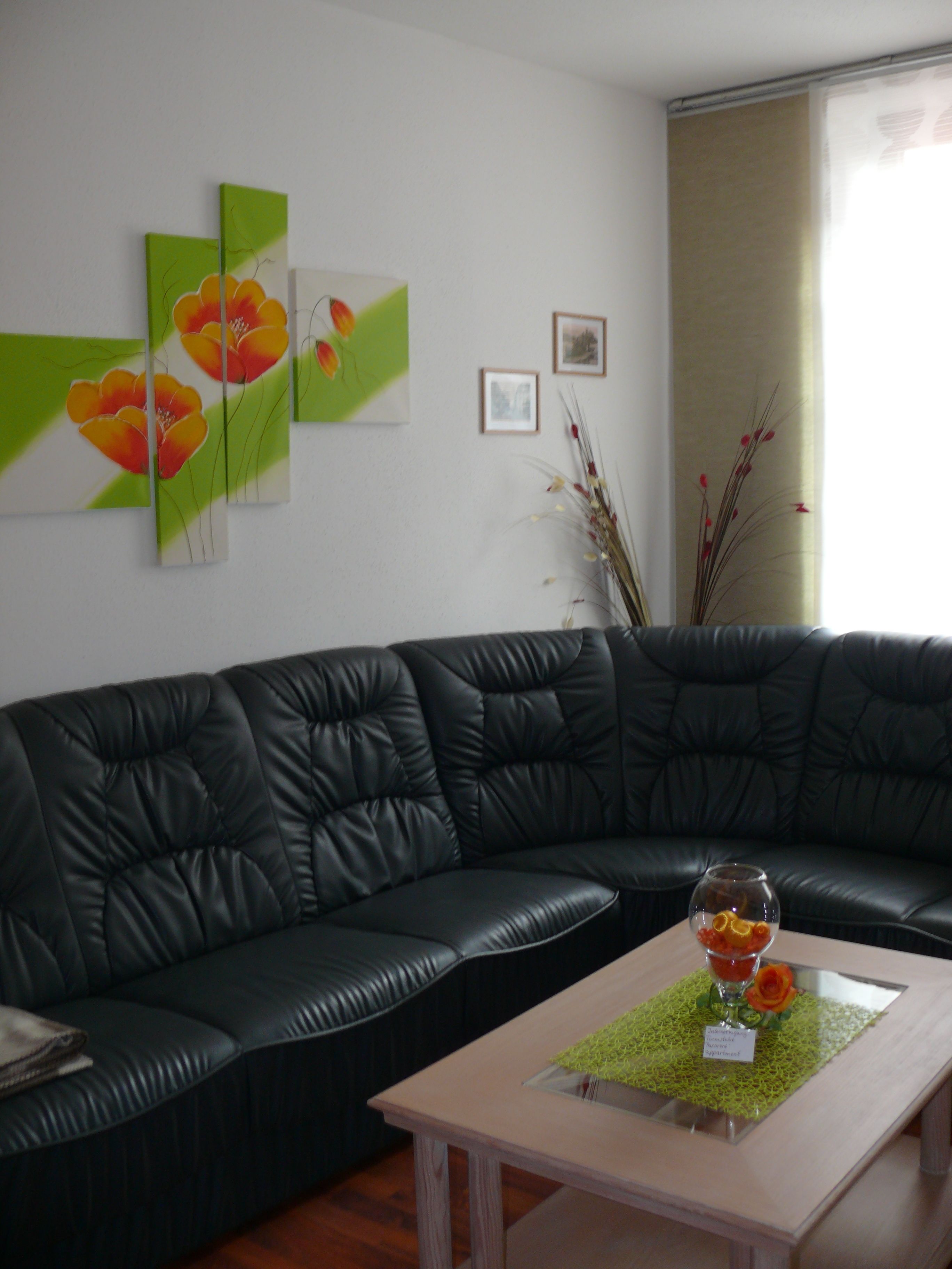Un salon moderne avec un canapé en cuir noir, une petite table basse en bois sur laquelle est posé un vase de fleurs, et des œuvres d’art accrochées au mur.