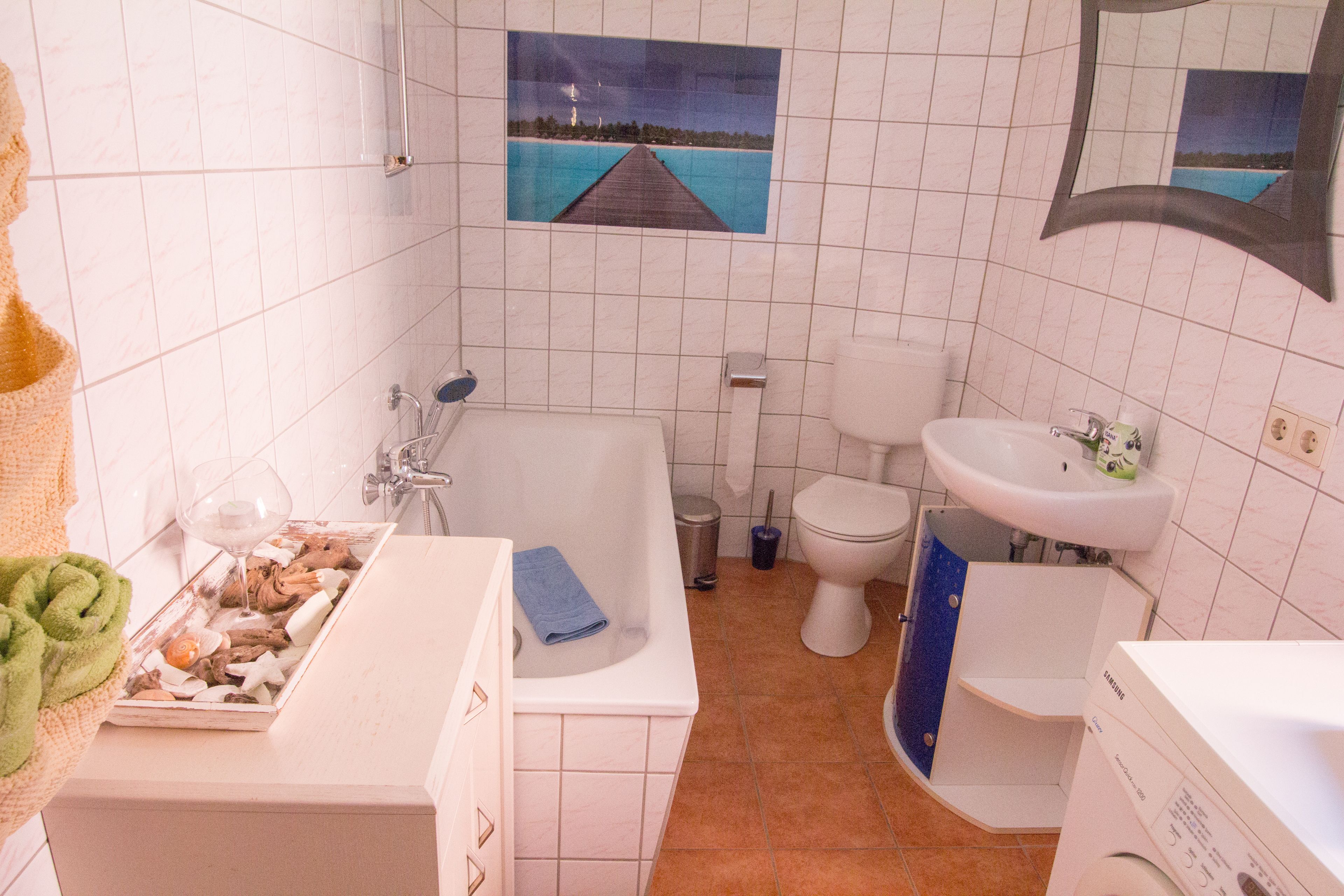 A bathroom with a bathtub, toilet, sink, and a small window with a view of the sea.