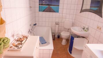 A bathroom with a bathtub, toilet, sink, and a small window with a view of the sea.