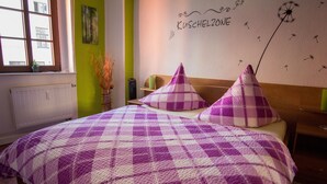 Un dormitorio con colcha de cuadros morados y blancos, pared verde y ventana con vistas.